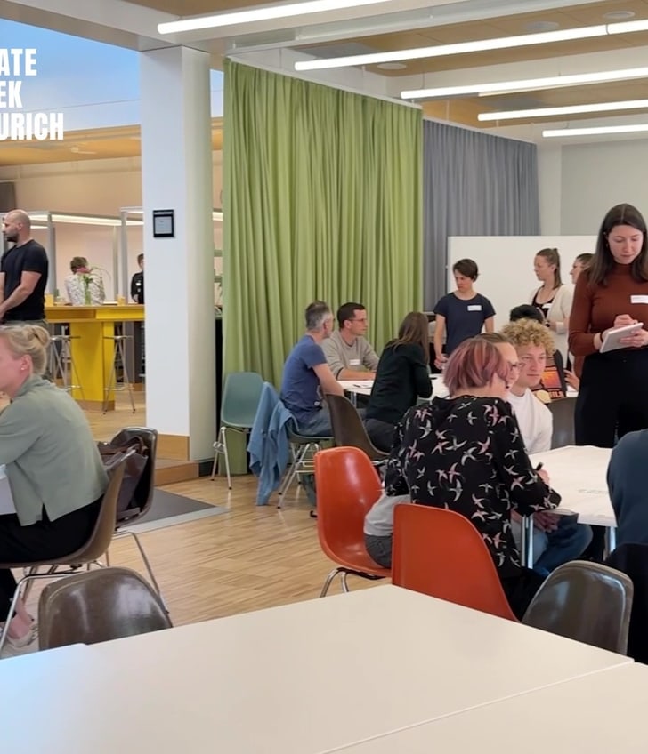 Menschen sitzen an Tischen bei Veranstaltung 'Climate Week Zurich'.