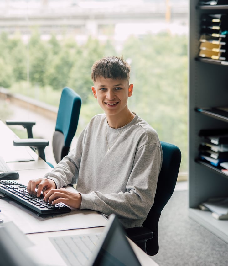 Junger Mann sitzt am Schreibtisch mit Computern im Büro.