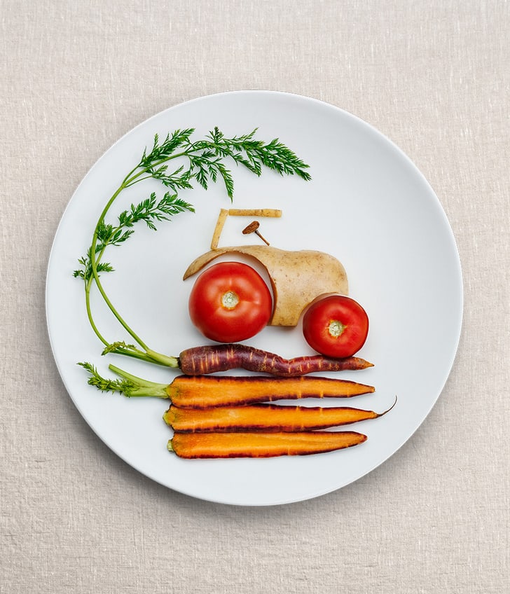 Teller mit Gemüse darauf, das aussieht wie ein Traktor und Karotten als Untergrund.