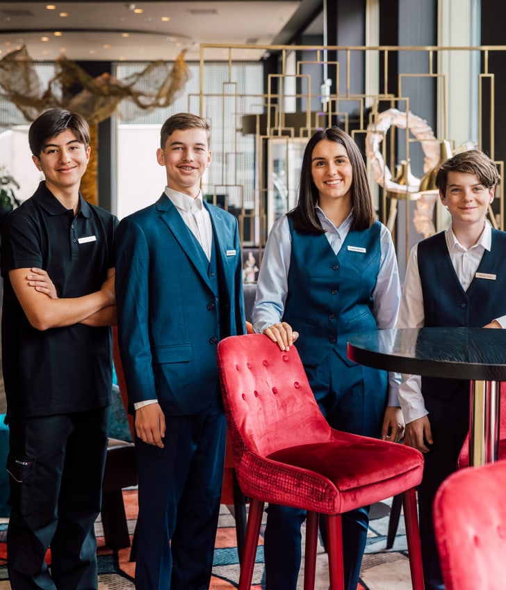 Vier Jugendliche in Restaurantuniformen posieren am Tisch in einem modernen Restaurant.