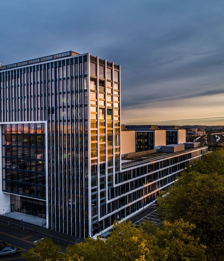 Hochhaus bei Sonnenuntergang mit Bäumen und Autos.