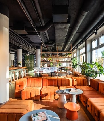 Modernes Café mit orangen Sofas und grossen Fenstern.