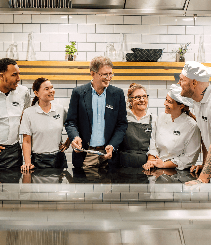 Gruppe von Menschen in Arbeitskleidung lachend in einer Küche.