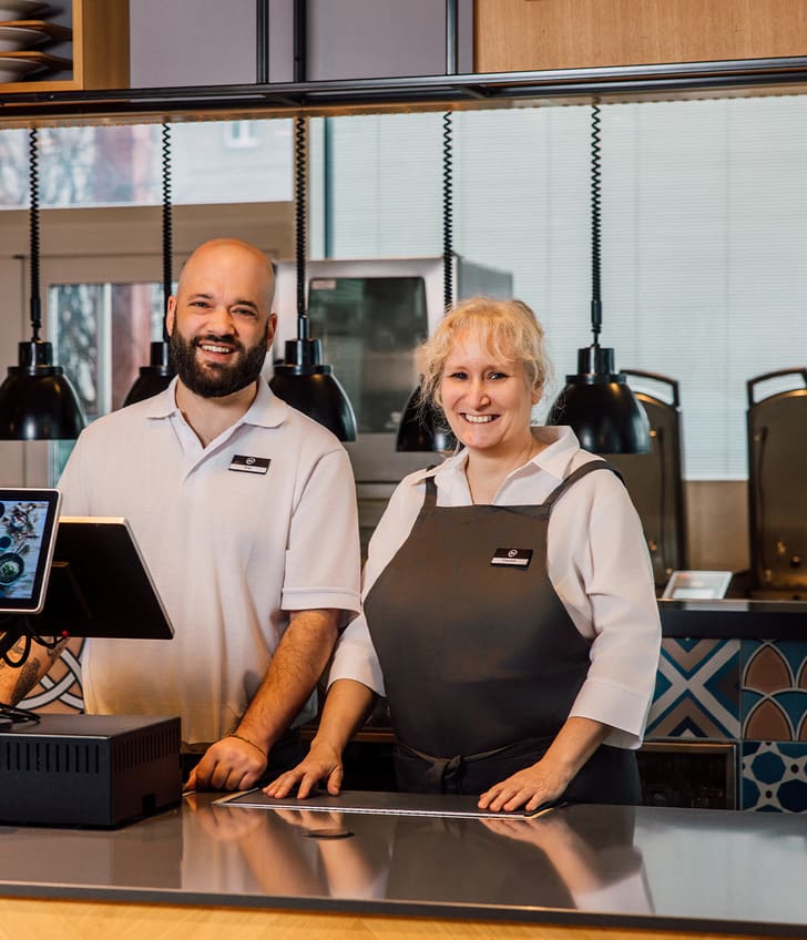 Zwei Personen stehen an einem Restauranttresen mit Kasse.