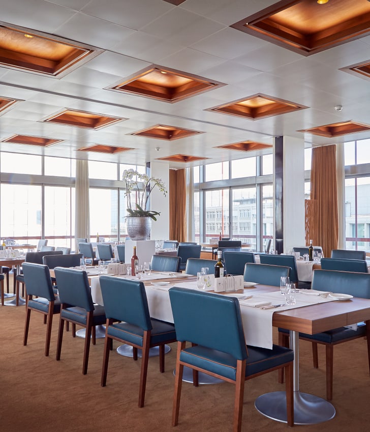 Modernes Restaurant mit blauen Stühlen und Tischen, grosse Fenster.