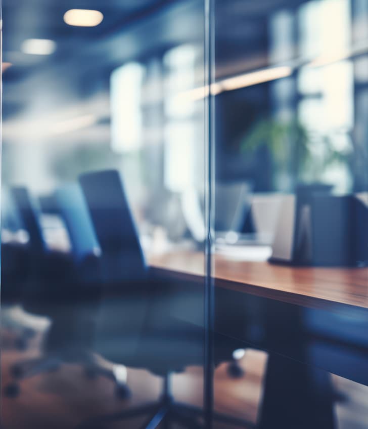 Moderne Büroinnenansicht durch Glas mit reflektierenden Oberflächen und Computerarbeitsplätzen.