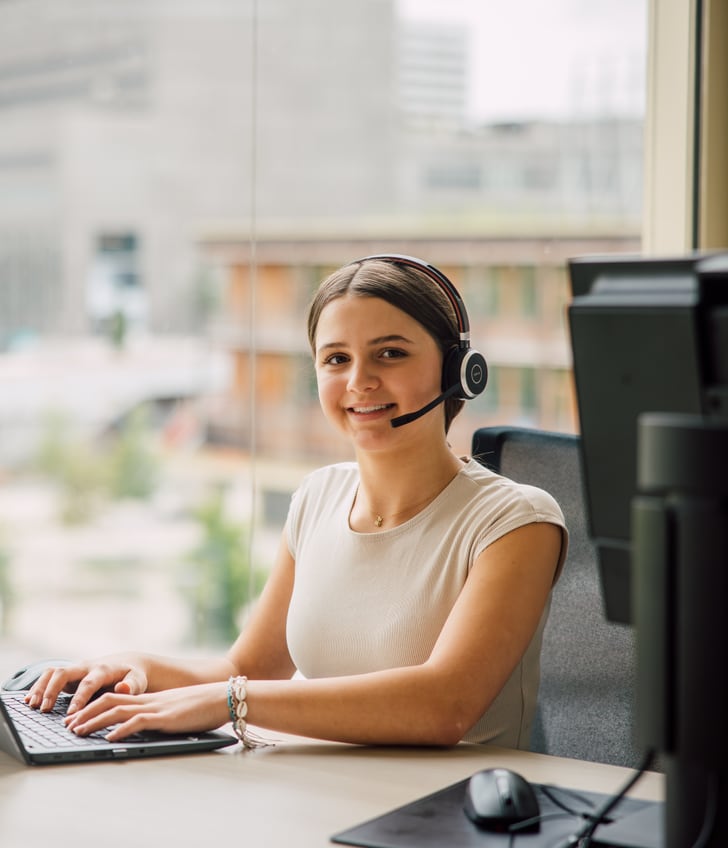 Frau mit Headset arbeitet am Laptop im Büro.