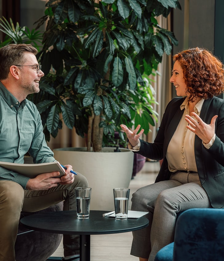 Mann und Frau bei Gespräch in modernem Büro, Pflanzen im Hintergrund.