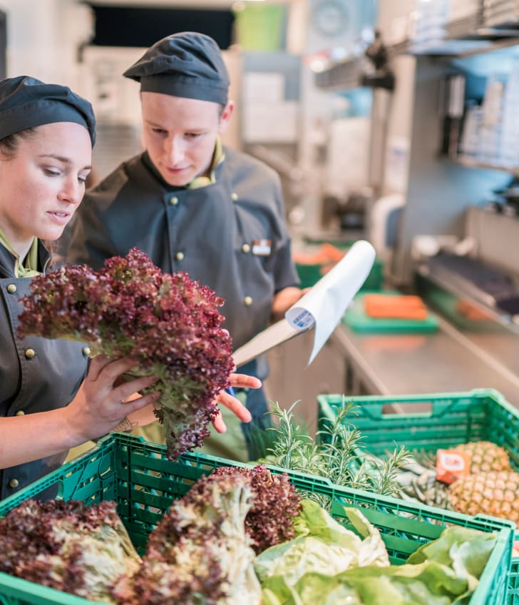 Zwei Mitarbeitende in der Küche kontrollieren die Lieferung von frischen Zutaten wie Salat und Früchten.