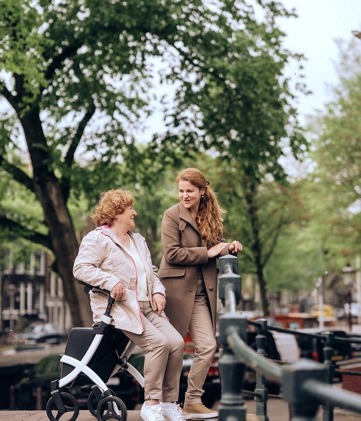 Ältere Frau mit Rollator und junge Frau gehen an einem Kanal entlang.