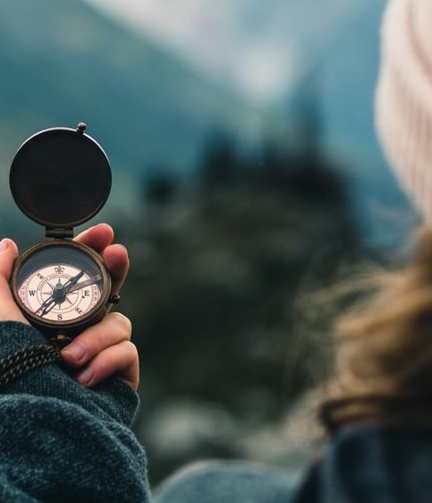 Frau von hinten, die einen Kompass in den Bergen hält