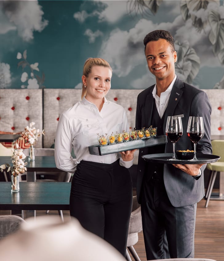 Zwei Kellner im eleganten Restaurant tragen Tabletts mit Getränken und Speisen.