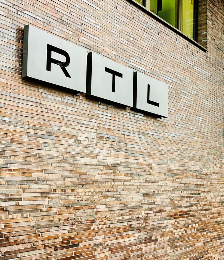 Backsteinwand mit RTL-Logo und Glastür.",