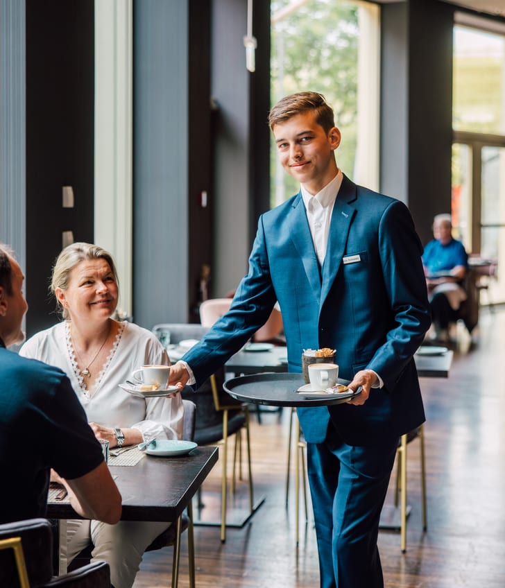 Lernender serviert Kaffee an Tisch in einem Café.