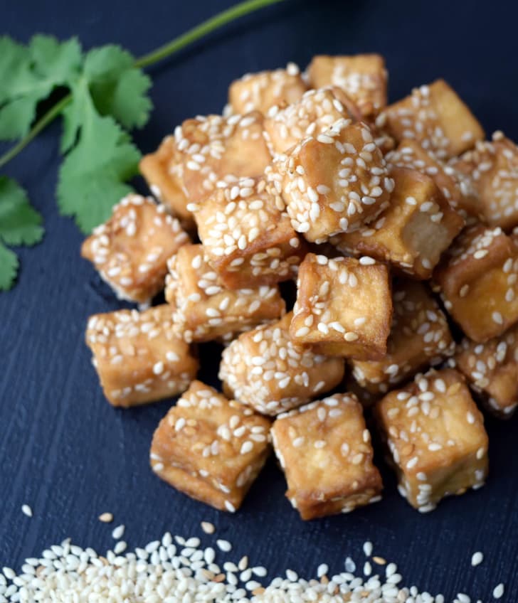 Gebratene Tofuwürfel mit Sesam, Korianderzweig im Hintergrund.