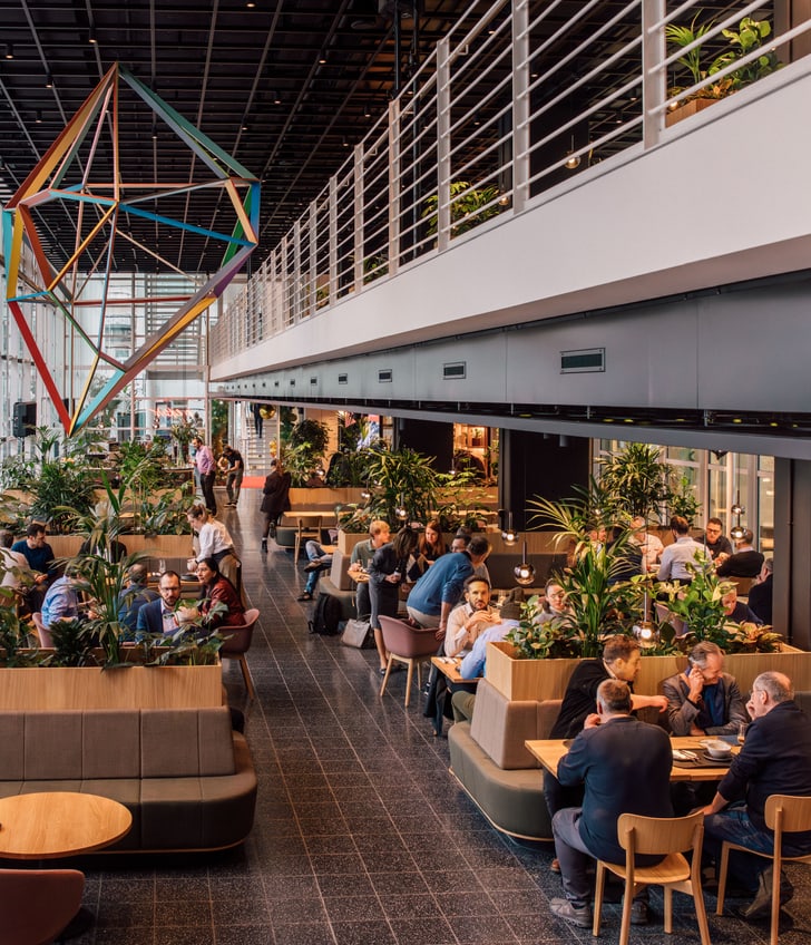 Geschäftsleute in modernem Café mit geometrischem Kunstwerk und Pflanzen.