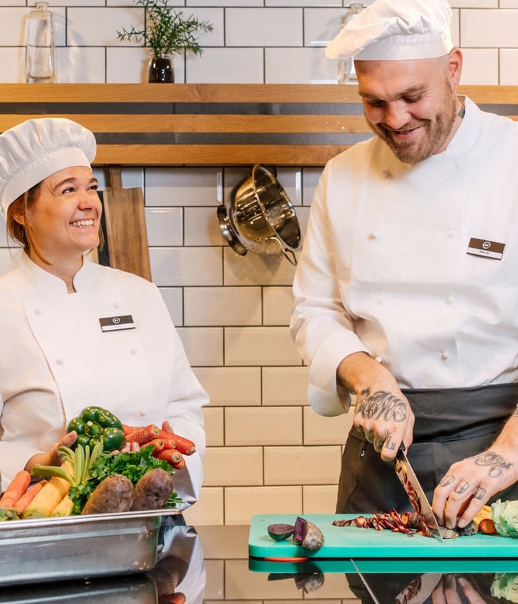 Zwei Köche schneiden Gemüse in der Küche, lachend und lächelnd.