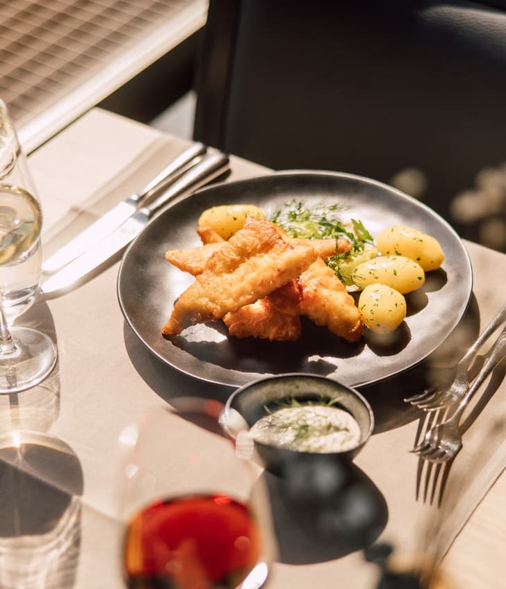 Gebratener Fisch mit Kartoffeln auf einem Teller, Wein und Wasser im Glas.