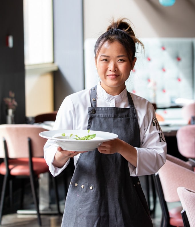 Köchin in schwarzer Schürze hält Teller mit Essen im Restaurant.