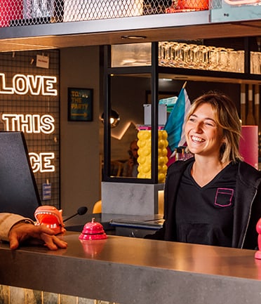 Frau lächelt an Empfangstresen mit Neonzeichen im Hintergrund.