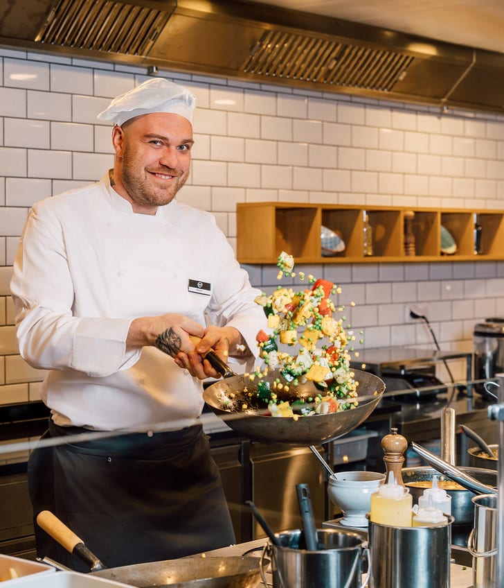 Koch in der Küche wirft Gemüse in einer Pfanne in die Luft.
