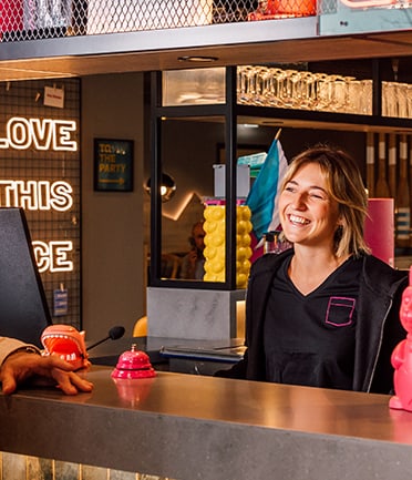 Frau lächelt an Empfangstresen mit Neonzeichen im Hintergrund.