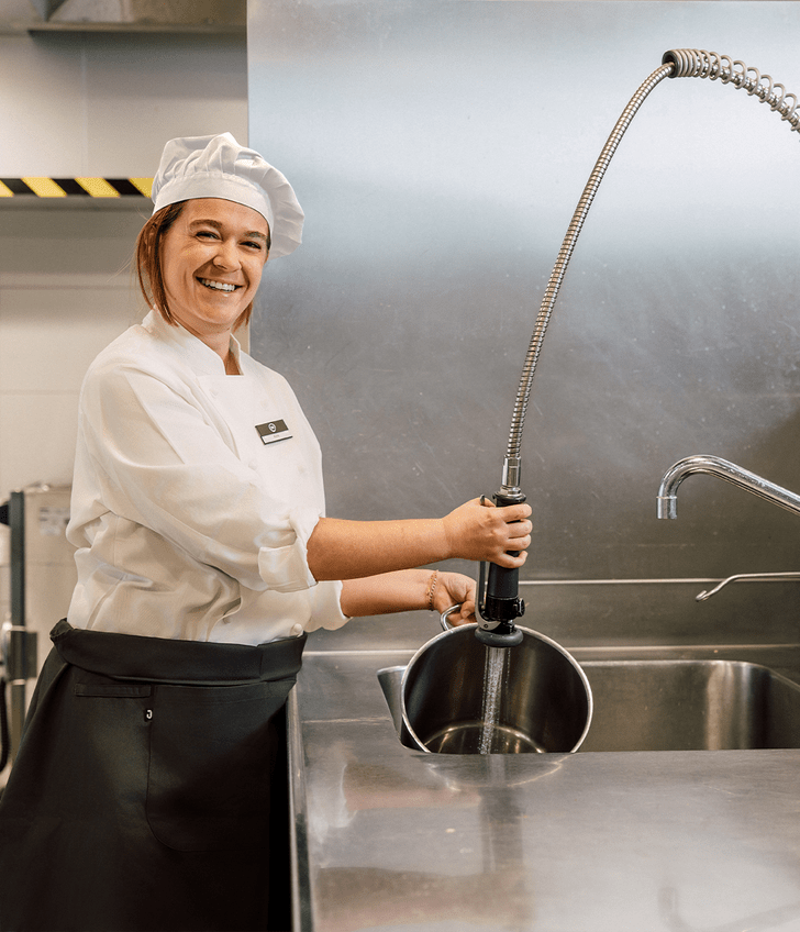 Lächelnde Köchin wäscht einen Topf in der Küche.