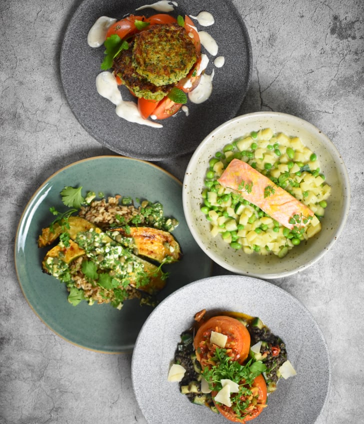 4 farbige Teller mit verschiedenem Essen darauf und grauem Untergrund