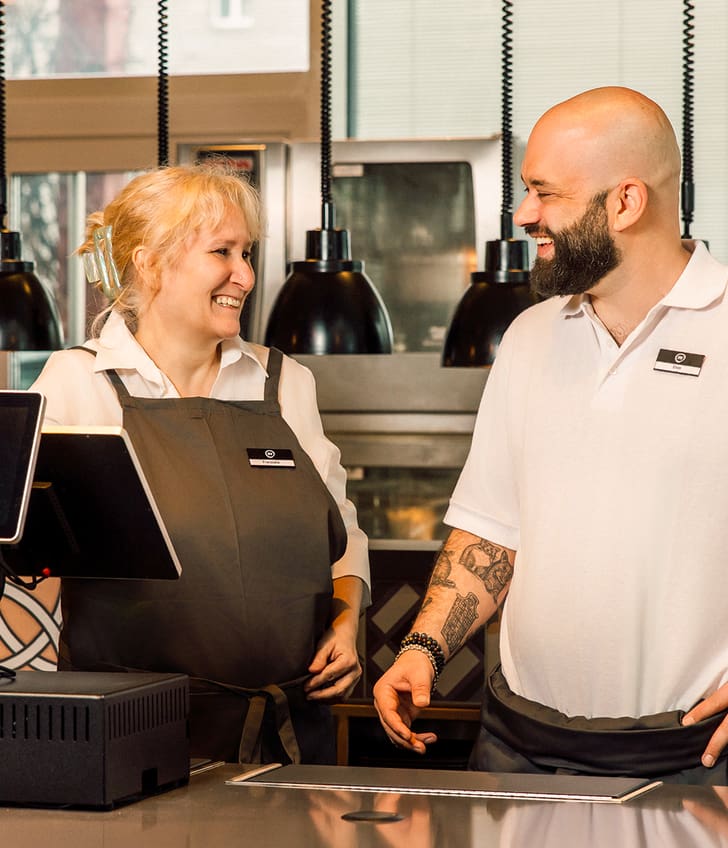Zwei lächelnde Mitarbeiter im Restaurant hinter der Theke.