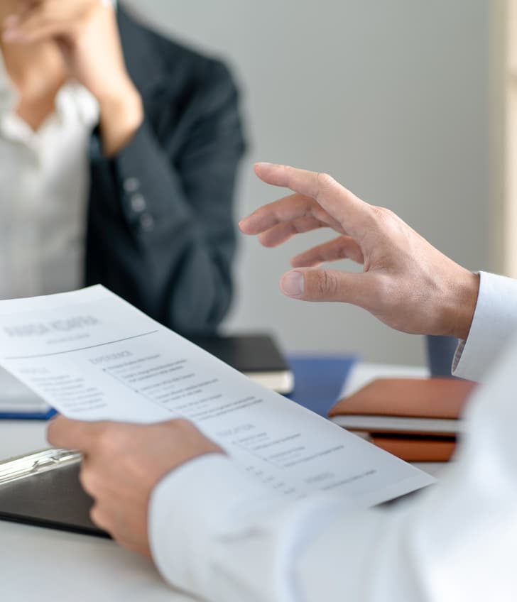 Bewerbungsgespräch mit zwei Personen und einem Lebenslauf auf einem Tisch.