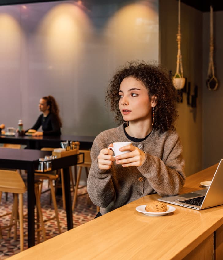 Person trinkt Kaffee in modernem Café mit Laptop.