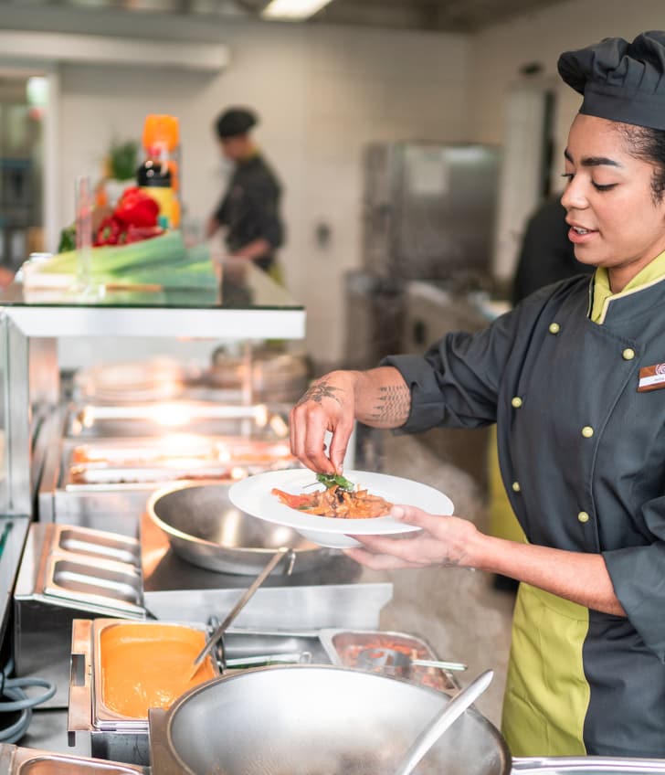 Köchin in Uniform bereitet Essen in einer Grossküche zu.