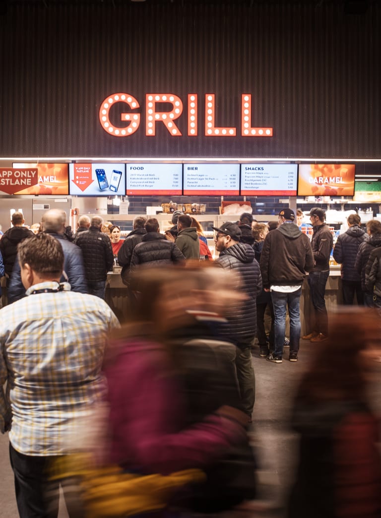 Belebte Szene vor einer Essenstation im Stadion an einem Eishockey Match in der Swiss Life Arena in Altstetten Zürich, wo die Fans auf ih Essen warten.
