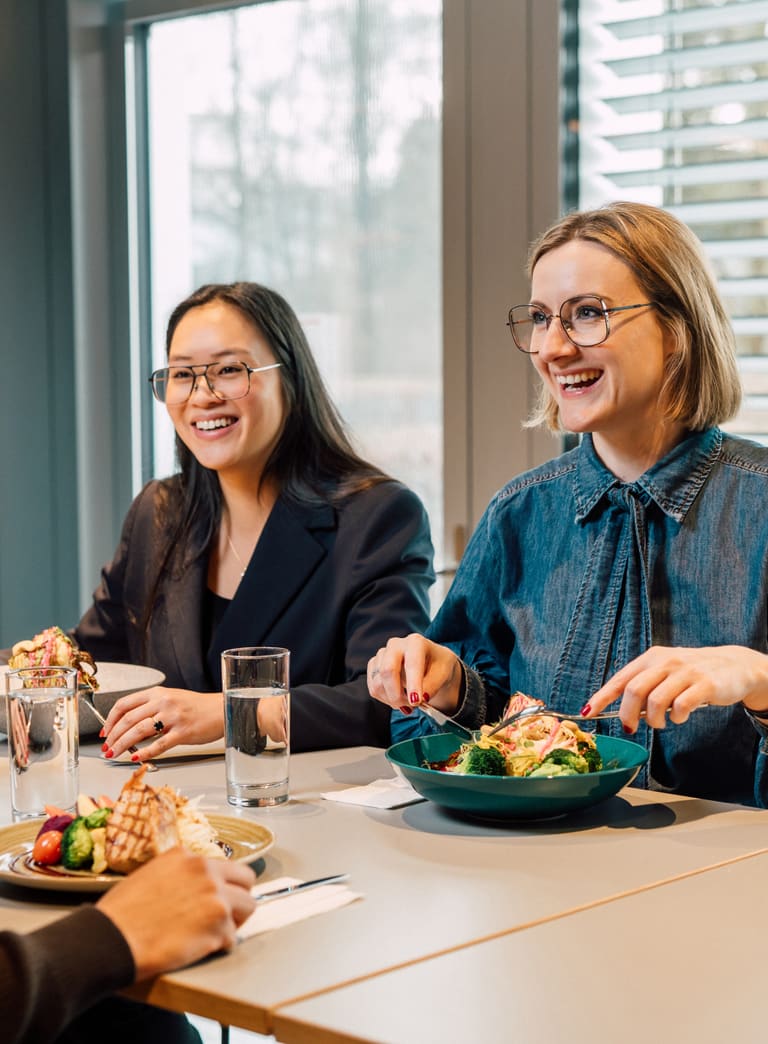 Drei Personen beim Mittagessen in einem Restaurant lächelnd am Tisch.