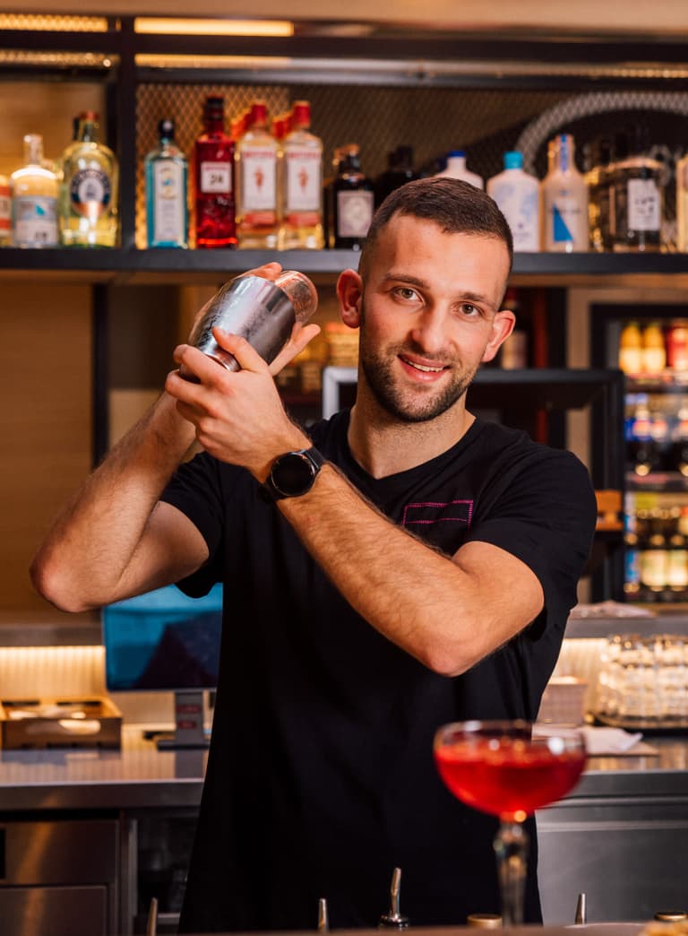 Barkeeper hält Shaker hinter der Bar mit Getränken im Hintergrund.