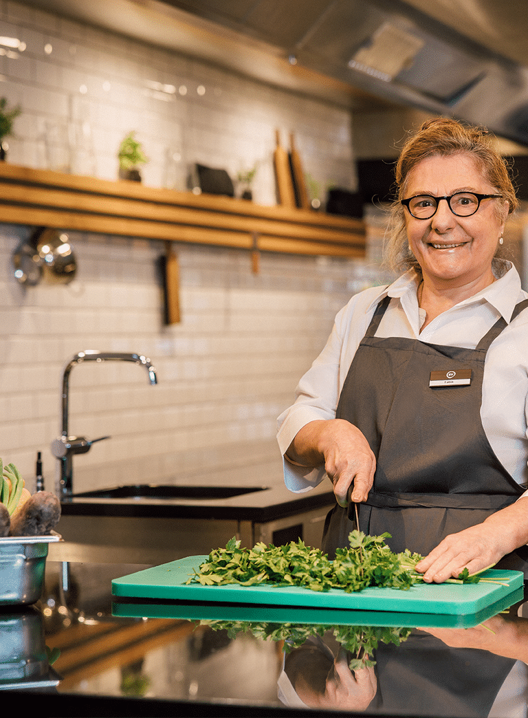 Köchin in Küche schneidet Kräuter auf grünem Schneidebrett.