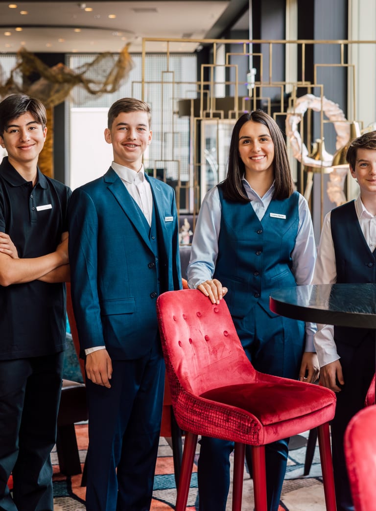 Vier Jugendliche in Restaurantuniformen posieren am Tisch in einem modernen Restaurant.