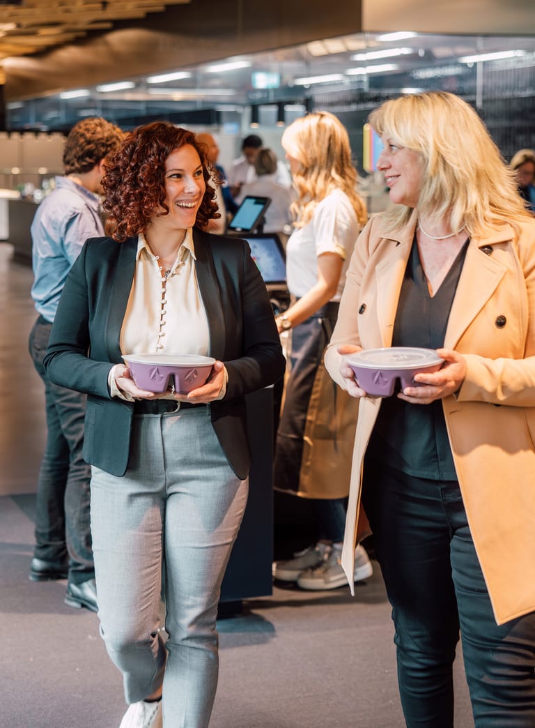 Zwei Frauen gehen mit Tabletts in einem modernen Bürorestaurant.