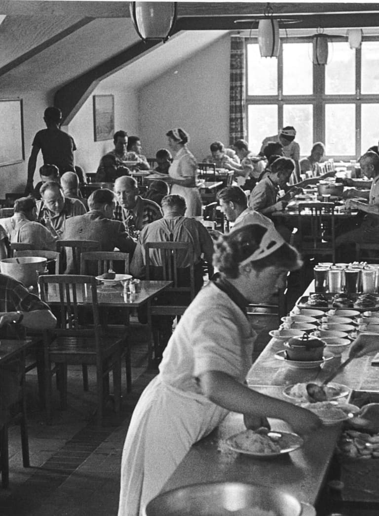 Historisches Foto eines Personalrestaurants in schwarz-weiss, wo viele Menschen beim Mittagessen sitzen und im Vordergrund an der Theke geschöpft wird.