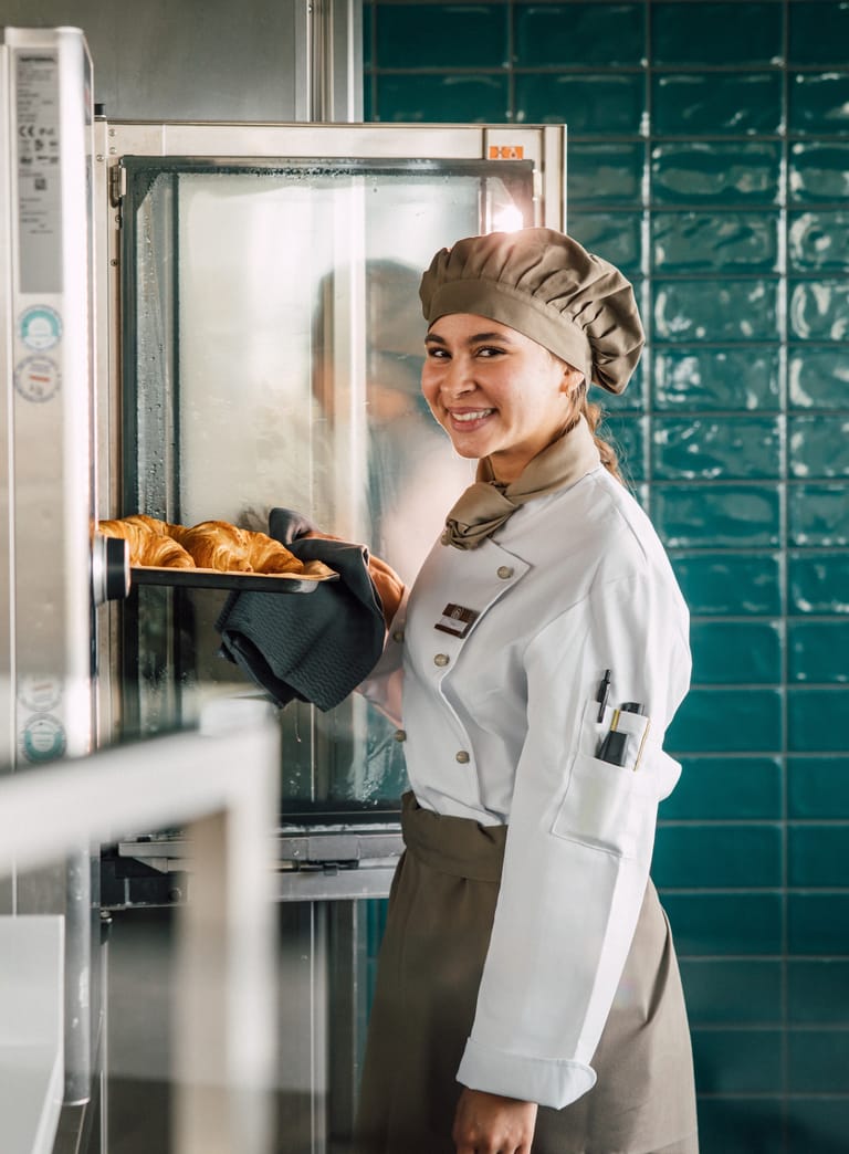 Köchin nimmt Croissants aus dem Ofen in der Küche heraus.