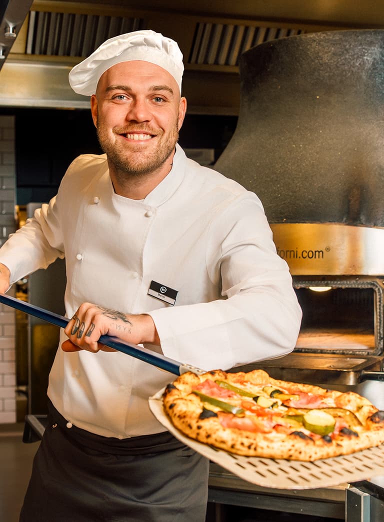 Koch im weissen Outfit hält Pizzaheber mit Pizza.