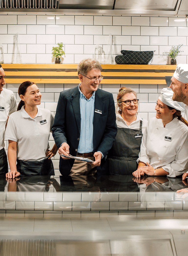 Gruppe von Menschen in Arbeitskleidung lachend in einer Küche.
