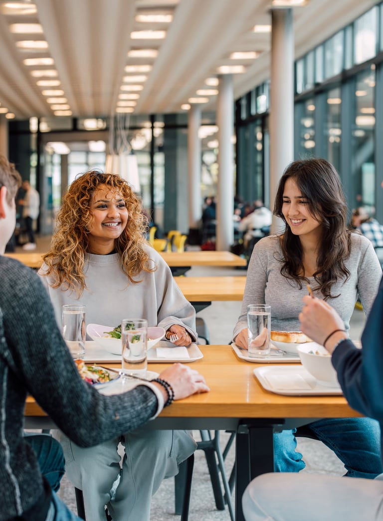 Gruppe von vier Personen sitzt und unterhält sich an einem Tisch in einer hellen Cafeteria