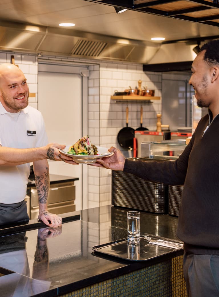 Koch überreicht Gast einen Teller in der Küche.