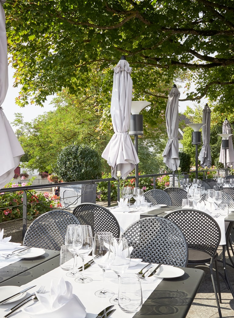 Sommerterrasse auf dem Schloss Laufen am Rheinfall unter Bäumen und weiss gedeckte Tische.