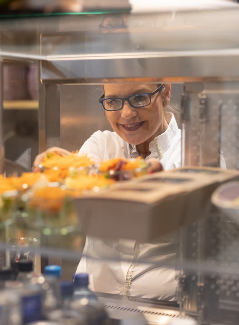 Koch hinter einer Vitrine mit Essen.