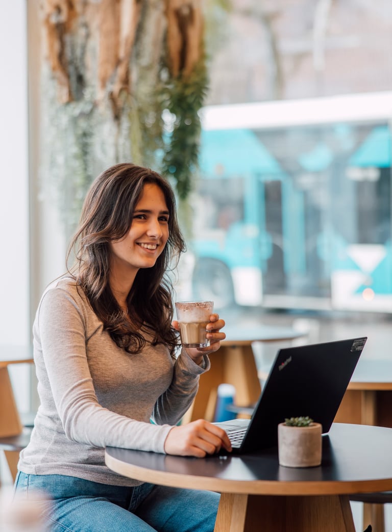 Frau mit Laptop und Kaffee sitzend an einem Café-Tisch.
