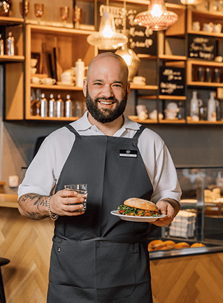 Mann im Café hält Teller mit Sandwich und Glas Wasser.