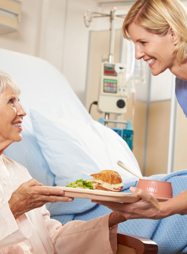 Krankenschwester serviert älterer Patientin im Krankenhauszimmer Essen.