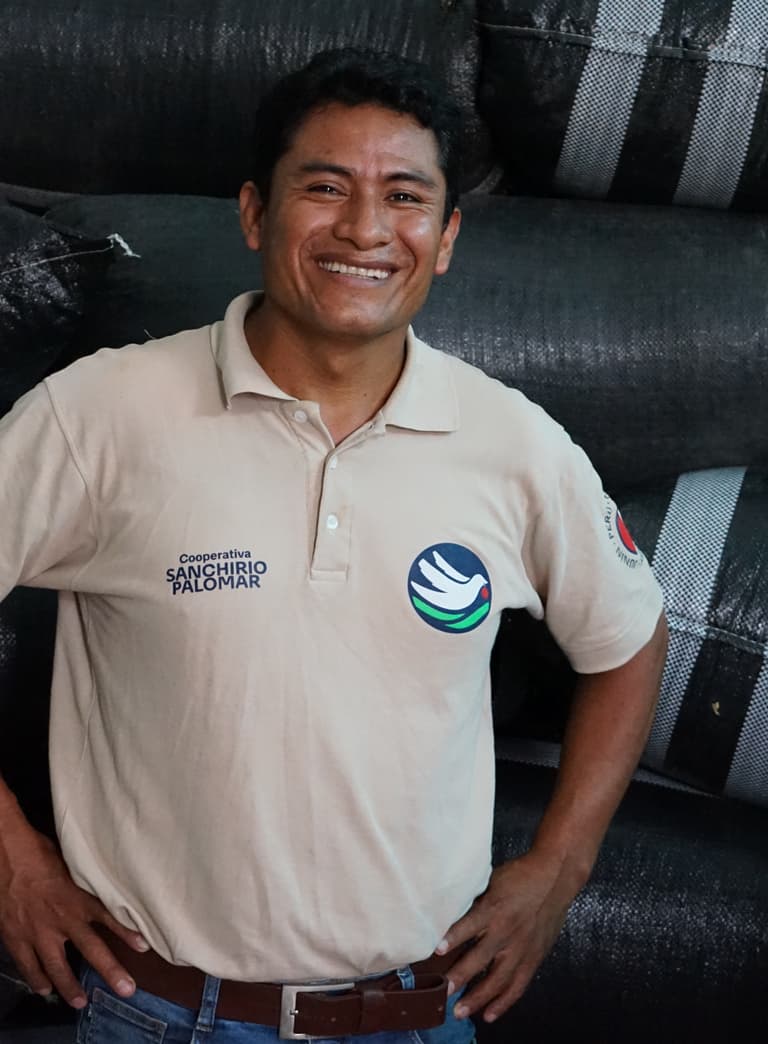 Mann lächelnd vor gestapelten Säcken.",